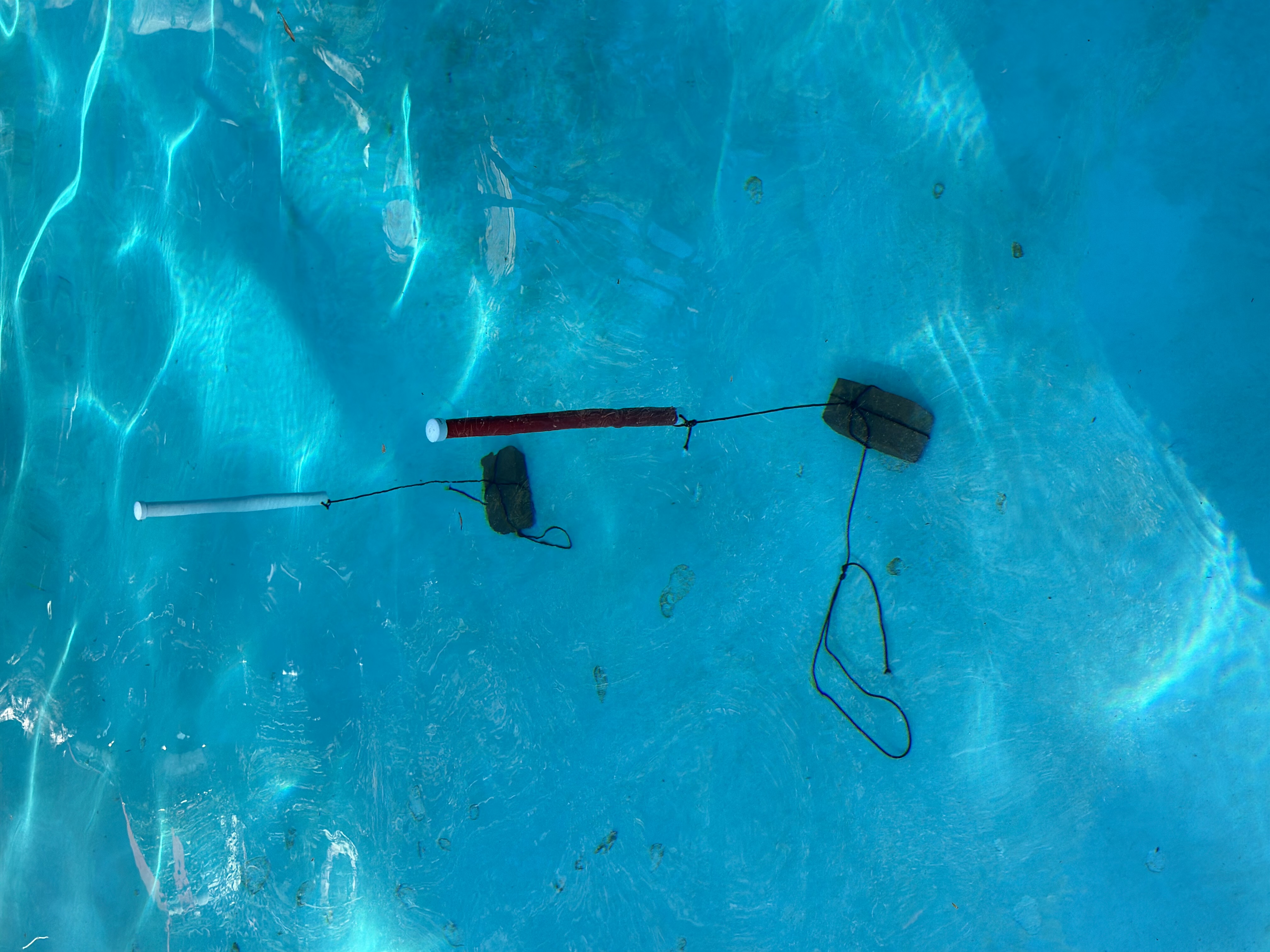 Weighted white and red PVC markers staked to the pool bottom forming a stand-in competition gate during the June 23, 2026 wet test.